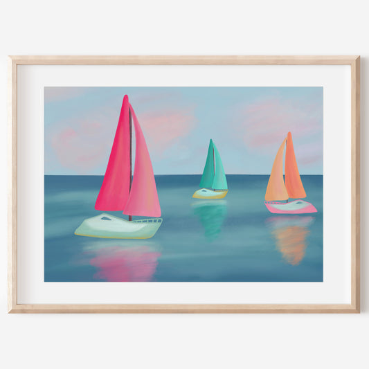 A framed art print depicting three colorful sailboats on a calm blue sea under a pastel sky, presented in a light wood frame with a white mat.
